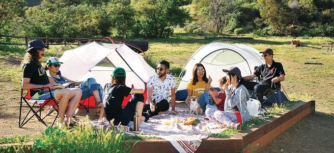 ロサンゼルスのキャンプでテントを張って団らんする人々