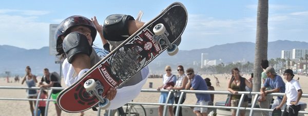 ロサンゼルスのベニスビーチでスケートボードを遊ぶ少年と観光客